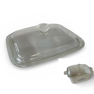 May include: A clear glass rectangular casserole dish lid with a rounded knob handle. The lid is designed to fit a square or rectangular baking dish. A smaller, matching casserole dish is also visible.