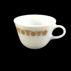May include: White ceramic coffee mug with a gold floral pattern around the rim.