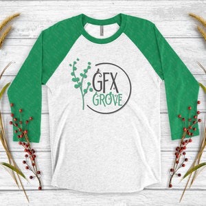 May include: A white and green baseball tee shirt with a green and black logo that says "GFX GROVE" in a circle. The logo is centered on the shirt.