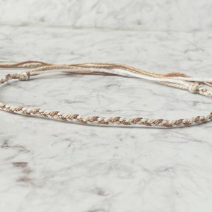 Op de afbeelding: Een gevlochten armband van wit en gouden koord. Het koord is gedraaid en heeft een subtiele glans.