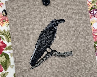 Broderad bokomslag med korpmotiv