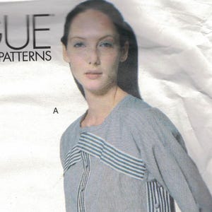 Puede incluir: Patrones Vogue diseño Issey Miyake. El patrón presenta un conjunto de dos piezas con una parte superior de manga larga y pantalones. La parte superior y los pantalones son grises con detalles de rayas verticales y horizontales. Talla 14.