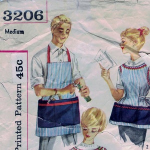 May include: A vintage Simplicity sewing pattern for two aprons. The pattern is for a striped apron with a pocket and a floral apron with a pocket. The pattern number is 3206 and the size is Medium. The pattern is printed on a white background with pink and blue text.
