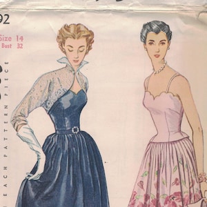 May include: Vintage Simplicity pattern book cover featuring two illustrated dresses. One is a dark blue dress with a lace bolero, the other is a pink floral dress. The text reads "Simplicity Printed Pattern 50c".