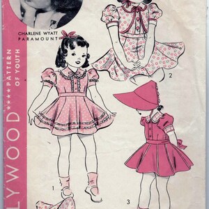 May include: A vintage sewing pattern for a girl's dress and hat. The pattern is for a 4-year-old and features a pink dress with white polka dots and a matching hat. The pattern is from the Hollywood Pattern Company and features a photo of actress Charlene Wyatt.