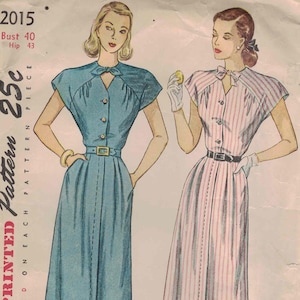 May include: A Simplicity sewing pattern envelope 2015 featuring illustrations of two dresses with short sleeves, button-front closures, and belted waists. One dress is solid blue, the other is pink and white striped. Text includes Bust 40, Hip 43.