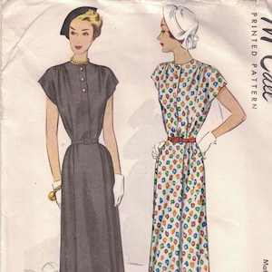 May include: Vintage McCall's printed pattern featuring two illustrations of maternity dresses. One dress is solid gray with a belt, the other is white with a colorful geometric pattern. The pattern is labeled "Maternity Dress".