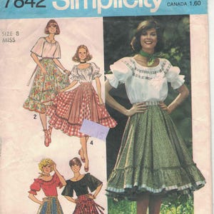 Puede incluir: Patrón de costura Simplicity vintage con talla 8 Miss. El patrón incluye ilustraciones de faldas y blusas de mujer en varios estilos. La imagen principal muestra a una mujer con una falda floral verde y una blusa blanca.