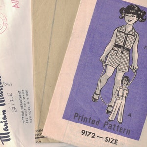 May include: A vintage sewing pattern for a girl's dress and matching doll outfit. The pattern is printed on a purple background and features a black and white illustration of a girl and a doll jumping rope. The pattern number is 9172 and the size is not specified.