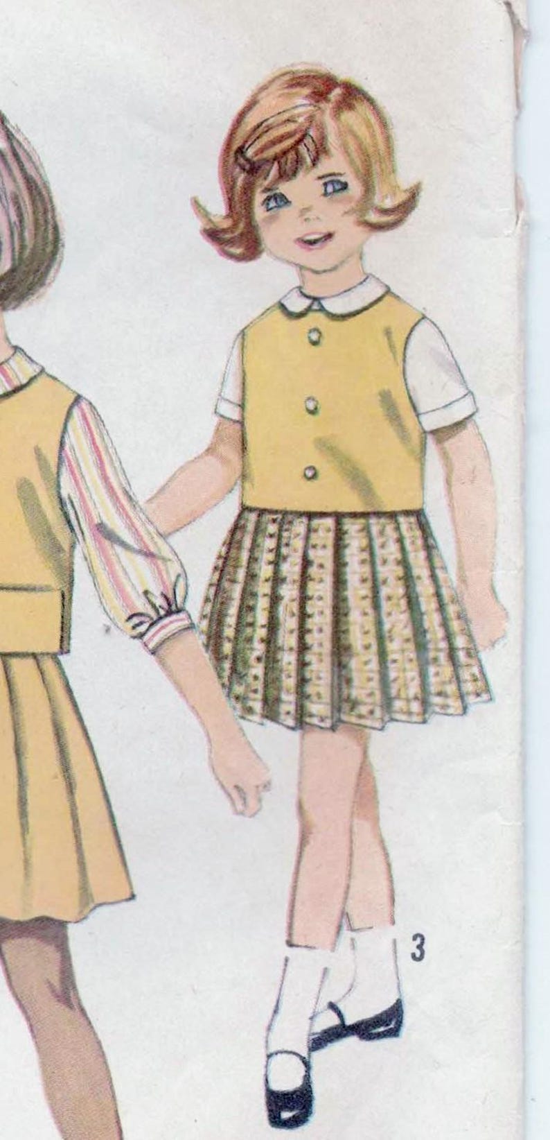 May include: A vintage illustration of two girls wearing matching yellow and brown dresses with white collars. The girl on the right has a short, blonde bob hairstyle and is wearing white socks and black shoes. The girl on the left has long, dark hair and is wearing a striped shirt. The illustration is from a vintage sewing pattern.