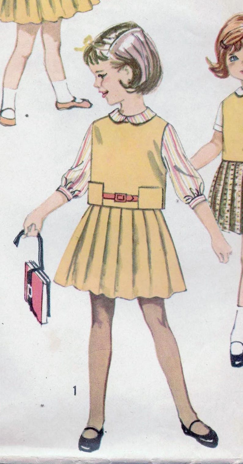 May include: A vintage sewing pattern for a girl's dress with a yellow skirt and a white blouse with a striped collar. The pattern includes a belt and a small purse.
