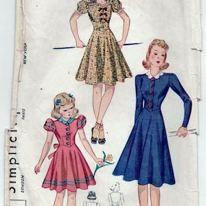 May include: Vintage sewing pattern for three dresses. The pattern is for a girl's dress with a floral print, a girl's dress with a solid pink color, and a woman's dress with a solid blue color. The pattern is from the company 'Simplicity' and is labeled '15c'.