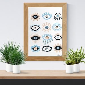 May include: A framed print with a pattern of stylized eyes in blue, beige, and black on a white background. The wooden frame surrounds the artwork. The print is displayed on a wooden shelf, accompanied by potted plants in white pots. The artwork is a decorative piece.