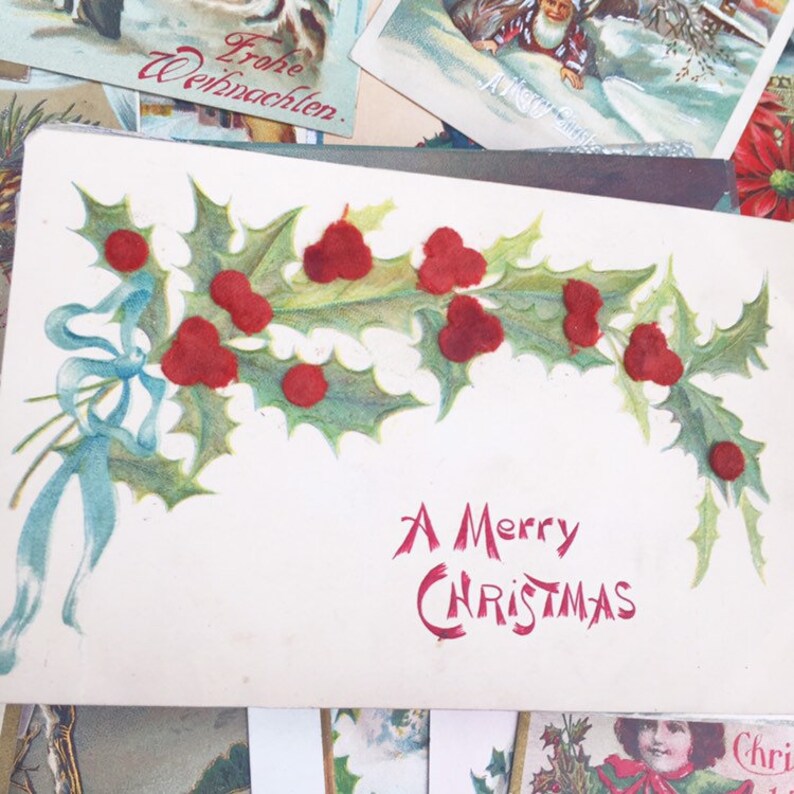 May include: A vintage Christmas postcard featuring a holly sprig with red berries. The text "A Merry Christmas" is written in red cursive.