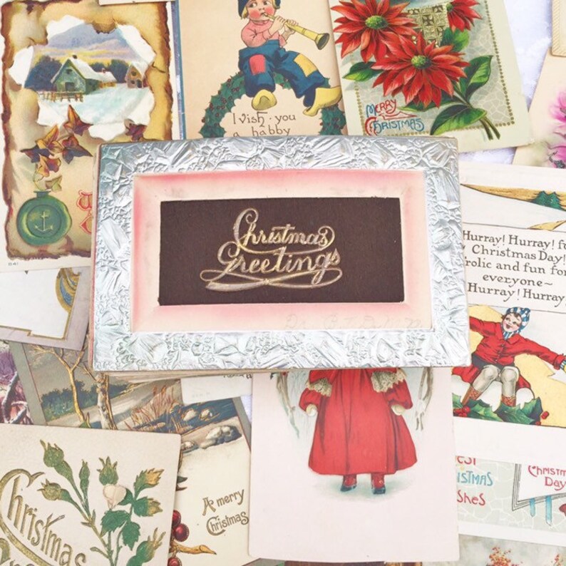 May include: A collection of vintage Christmas cards featuring a variety of designs, including a silver frame with the inscription "Christmas Greetings" in gold lettering.