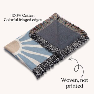 May include: A woven cotton throw blanket with a blue and beige sunburst design. The blanket has colorful fringed edges and the text "Woven, not printed". The blanket is made of 100% cotton.