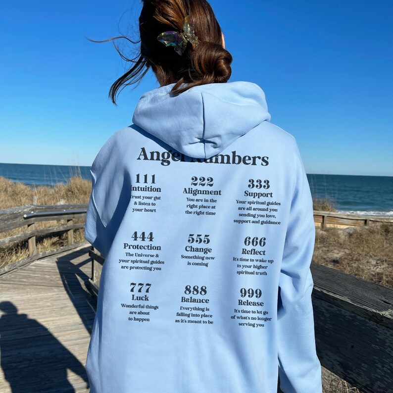 May include: Light blue hoodie with the text "Angels Numbers" and various number meanings printed on the back. The hoodie features a drawstring hood and long sleeves. The text includes numbers like 111, 222, 333, 444, 555, 666, 777, 888, and 999.