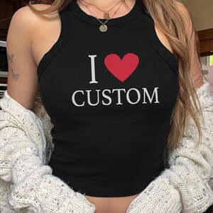 May include: Black tank top with the text "I &hearts; CUSTOM" in white and a red heart. The top is sleeveless and has a round neckline. The image shows the top on a person.