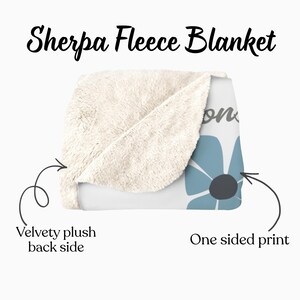 May include: A Sherpa fleece blanket with a velvety plush back side and a one-sided print. The blanket features a light blue flower design with a dark gray center on a white background. The text "Sherpa Fleece Blanket" is at the top.