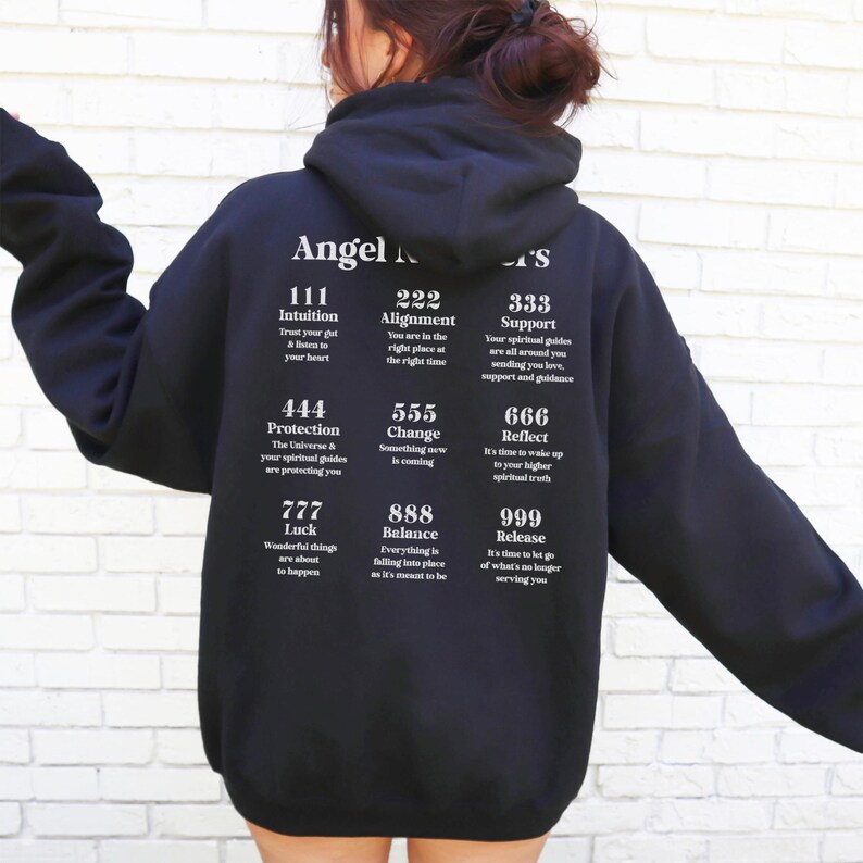 May include: Black hooded sweatshirt with white text. The text includes the words "Angel Numbers" and various number combinations with corresponding affirmations. The sweatshirt is a casual, comfortable style.