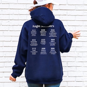May include: A navy blue hooded sweatshirt with the words "Angel Numbers" printed on the back. Below the text are various angel number meanings, including "111 Intuition" and "222 Alignment". The sweatshirt is made of a soft material.