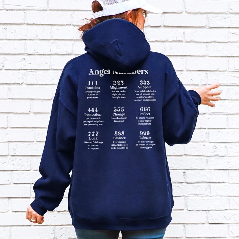 May include: A navy blue hooded sweatshirt with the words "Angel Numbers" printed on the back. Below the text are various angel number meanings, including "111 Intuition" and "222 Alignment". The sweatshirt is made of a soft material.