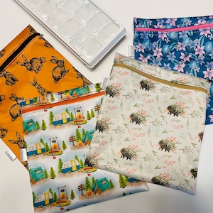 May include: Four reusable zippered bags with different patterns. One bag has a brown background with a white rabbit pattern. Another bag has a white background with a blue and yellow camper van pattern. A third bag has a white background with a brown hedgehog pattern. The fourth bag has a blue background with a pink flower pattern.