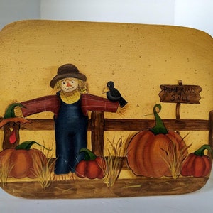 May include: A painted wooden sign with a scarecrow, pumpkins, and a bird. The sign says "Pumpkins for Sale".