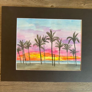 Puede incluir: Pintura acuarela de una puesta de sol sobre una playa con palmeras. El cielo es una mezcla de rosa, morado y naranja. El agua es de un azul profundo. Las palmeras están silueteados contra la puesta de sol.