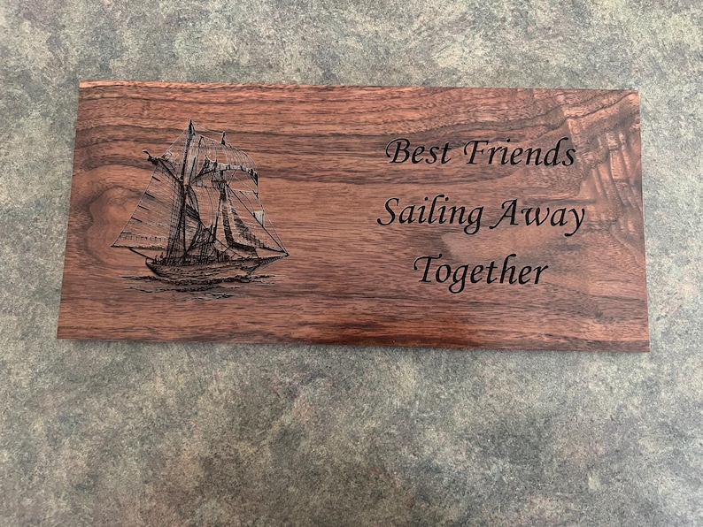 Op de afbeelding: Een houten plaquette met een gegraveerd beeld van een zeilboot en de tekst "Best Friends Sailing Away Together".