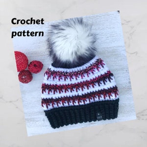 May include: A crochet hat with a white and red striped pattern and a black brim. The hat has a fluffy white pom pom on top. The hat is on a white wooden surface.