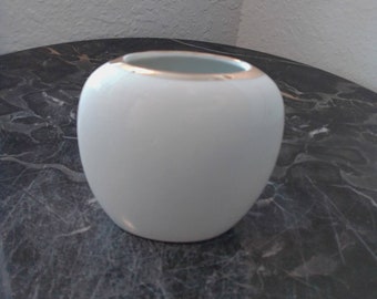 May include: A white ceramic vase with a gold rim. The vase is round and has a smooth surface.