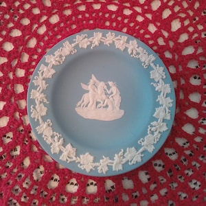 May include: A blue and white ceramic trinket dish with a white grapevine border and a raised white image of three figures in a classical scene.