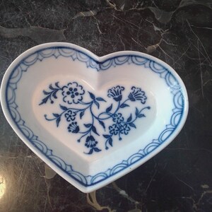 May include: A white heart-shaped dish with a blue floral design. The dish has a scalloped edge and is perfect for serving small treats or jewelry.