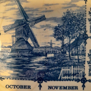 May include: A vintage blue and white calendar tile featuring a windmill, a bridge, and a house. The calendar shows the months of October and November with the days of the week and dates.
