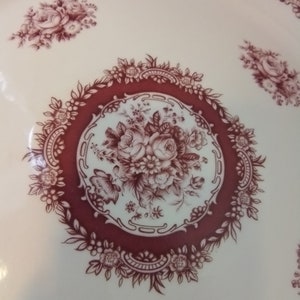 May include: A white ceramic plate with a burgundy floral design. The center of the plate features a large floral motif with a burgundy border.