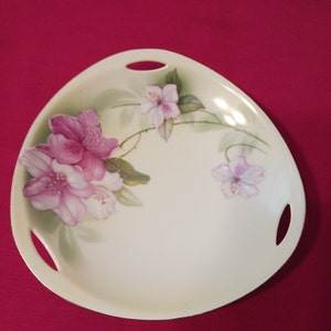 May include: A white oval serving dish with two handles. The dish is decorated with a floral design of pink and white flowers with green leaves.