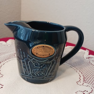 May include: A dark blue ceramic pitcher with a handle and a gold embossed label that reads "Royal Salute Blended Scotch Whisky".