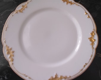 May include: A white porcelain plate with a scalloped edge and gold leaf accents. The plate has a simple, elegant design, with gold detailing around the rim. The plate is suitable for serving food.