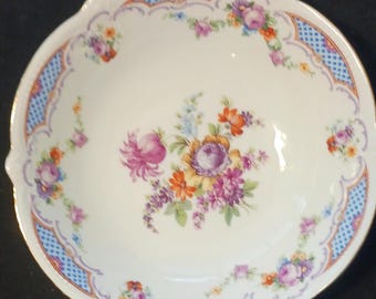 May include: A white porcelain bowl with a scalloped rim and a floral design. The bowl has a blue and white checkered border with a gold trim.