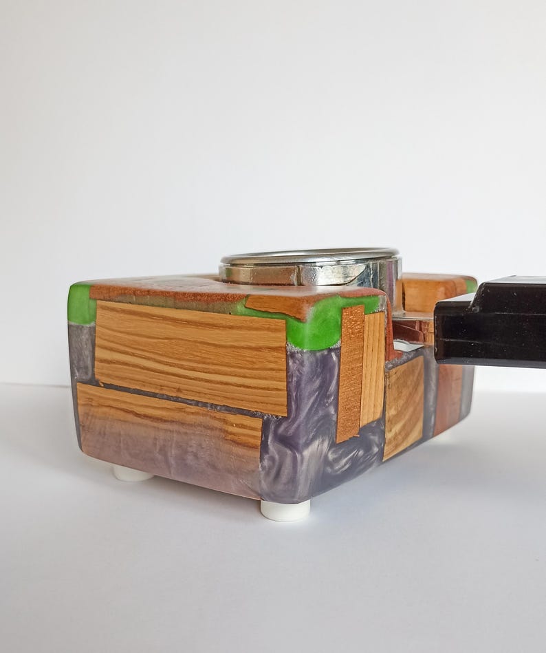May include: A handcrafted wooden box with a silver metal top and a black handle. The box is made of various wood pieces, green resin, and purple resin. It has white feet.