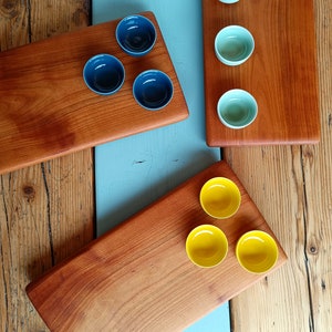 May include: Three wooden serving boards with various colored bowls. The boards are made of a light brown wood and have a smooth finish. The bowls are blue, green, and yellow.