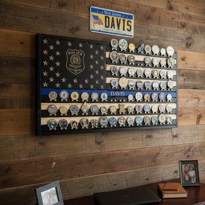 May include: A rectangular wooden wall display rack designed to hold challenge coins, featuring a black and natural wood flag pattern with a thin blue line. The display includes a police badge emblem, the name DAVIS, and numerous circular metal coins.