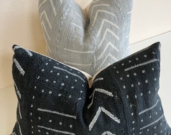 May include: Two decorative throw pillows. One is light gray with white chevron and line patterns. The other is black with white dot and arrow designs. Both pillows have a textured appearance and a neutral color palette.