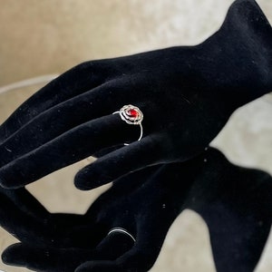 May include: A silver ring with a red gemstone set in a wire rose design.
