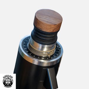 Puede incluir: Un molinillo de café negro con tapa de madera. El molinillo tiene un dial plateado con números y un fuelle de goma. El logotipo de Algovia Bear Upcycled Wood está en la esquina inferior izquierda.