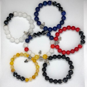 May include: Five bracelets with different colored beads and silver charms. The bracelets are made of white, blue, red, yellow, and black beads.