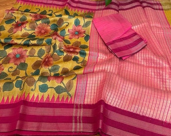 May include: A yellow and pink saree with a floral print. The saree has a pink border with gold accents. The saree is folded and laid out on a wooden floor.