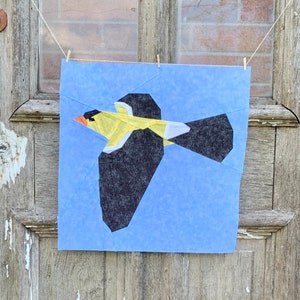 May include: A blue fabric panel with a black and yellow paper bird applique. The bird is flying with its wings spread. The fabric panel is hanging on a wooden door with a sign that says "America" above it.