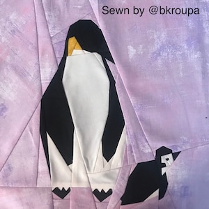May include: A purple fabric background with two black and white penguin appliques. The larger penguin is standing upright with its wings folded. The smaller penguin is facing the left side of the image. The text "Sewn by @bkroupa" is in the upper right corner of the image.